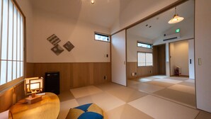 Una habitación con suelo de tatami, una mesa baja de madera, una lámpara y un mueble pequeño.