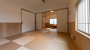 Un pasillo con suelo de tatami, puertas correderas y un ventanal con persianas verticales.