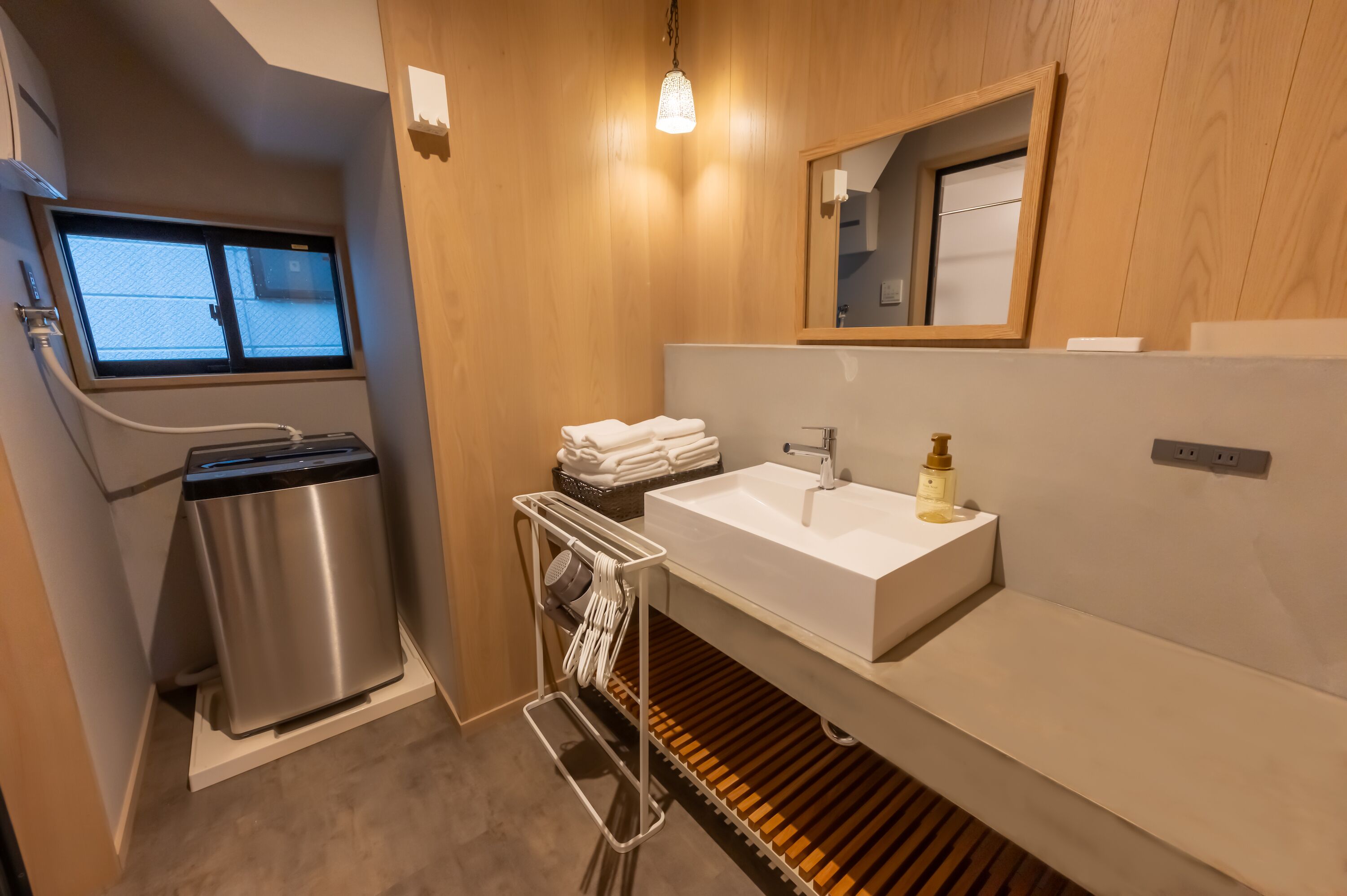A modern bathroom with a built-in sink, a trash bin, a towel rack, and a window.