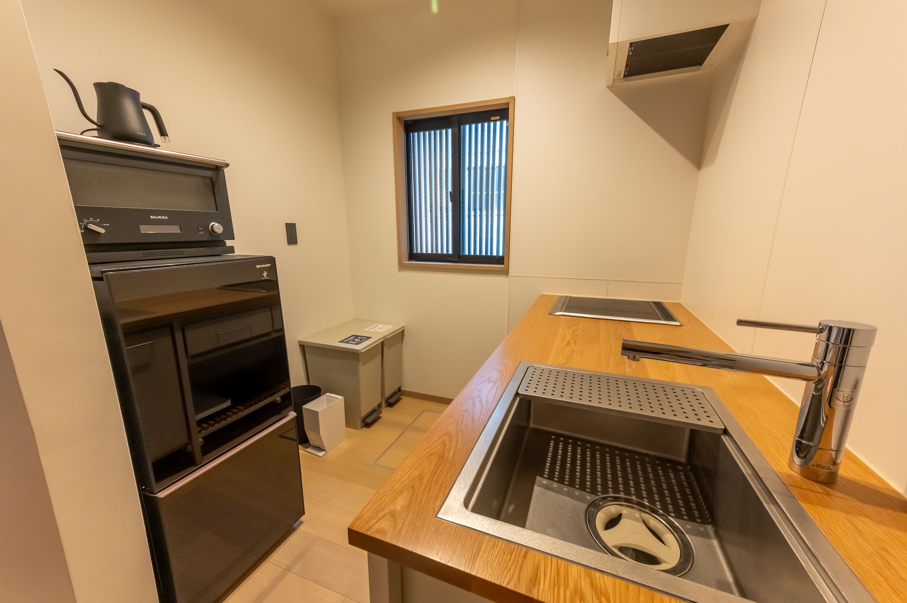 A compact kitchen with a built-in oven, a coffee maker, a window with blinds, a stainless steel sink, and a wooden countertop.