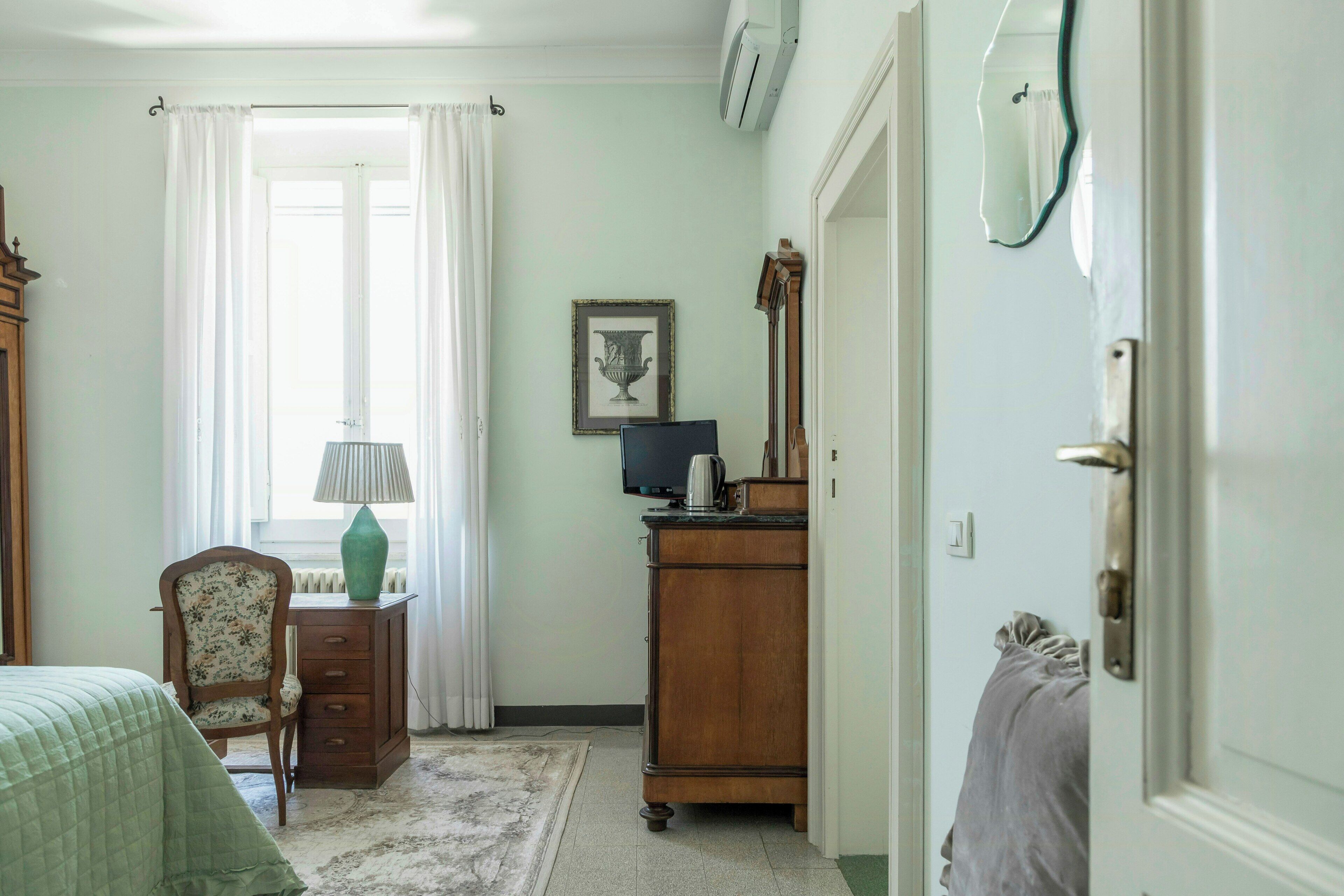 A bedroom with a bed, a chair, a dresser, a lamp, a framed picture, and a mirror.