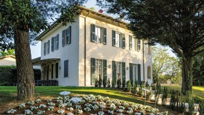 Un bâtiment à deux étages, doté d’une façade symétrique, d’un porche abrité et d’un jardin bien entretenu où poussent des fleurs blanches.