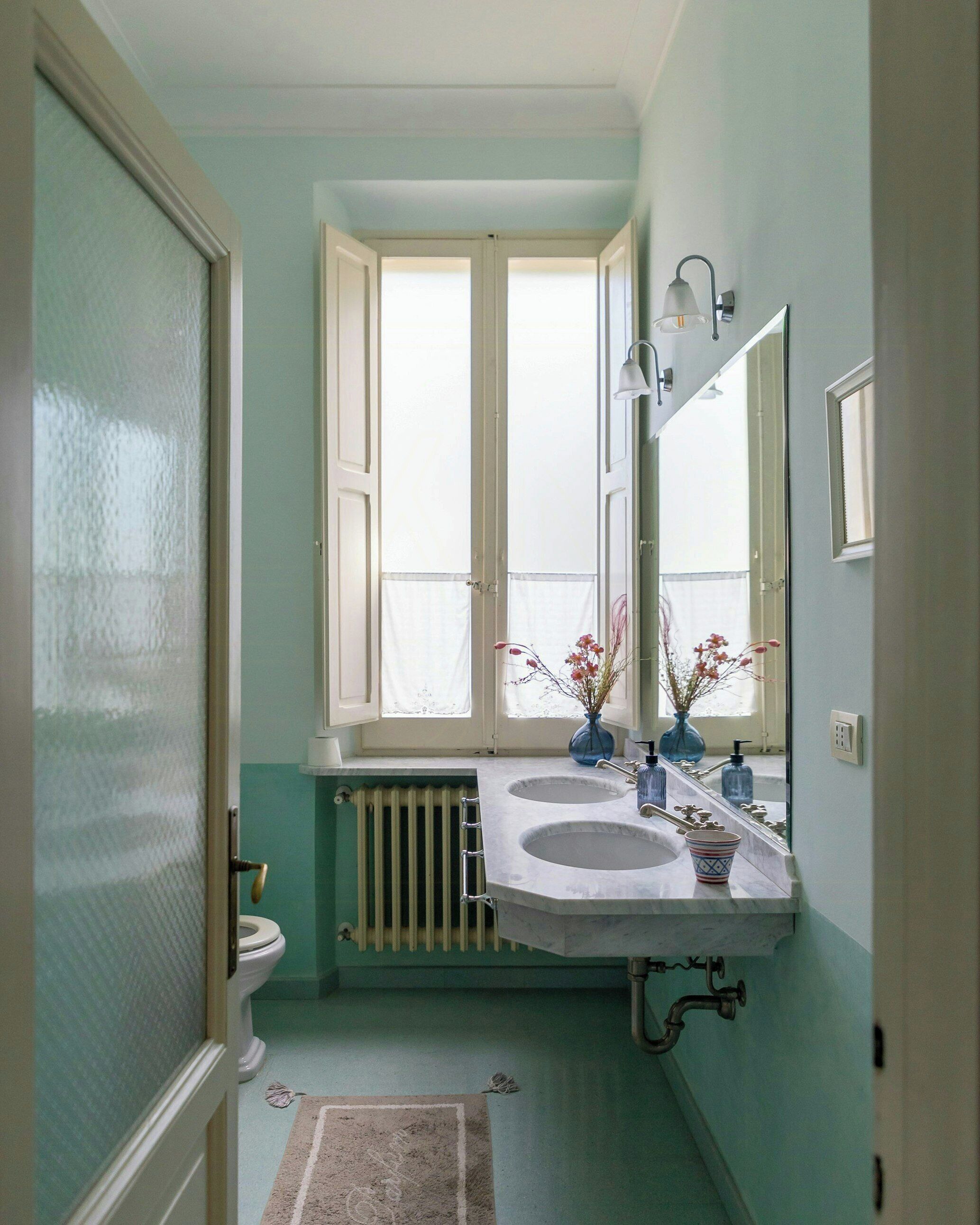 A bathroom with two sinks, a radiator, a window, and a mirror.