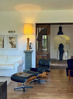 Ein Wohnzimmer mit einem weißen Sofa, einem schwarzen Ledersessel, einer Lampe und einem großen Fenster.