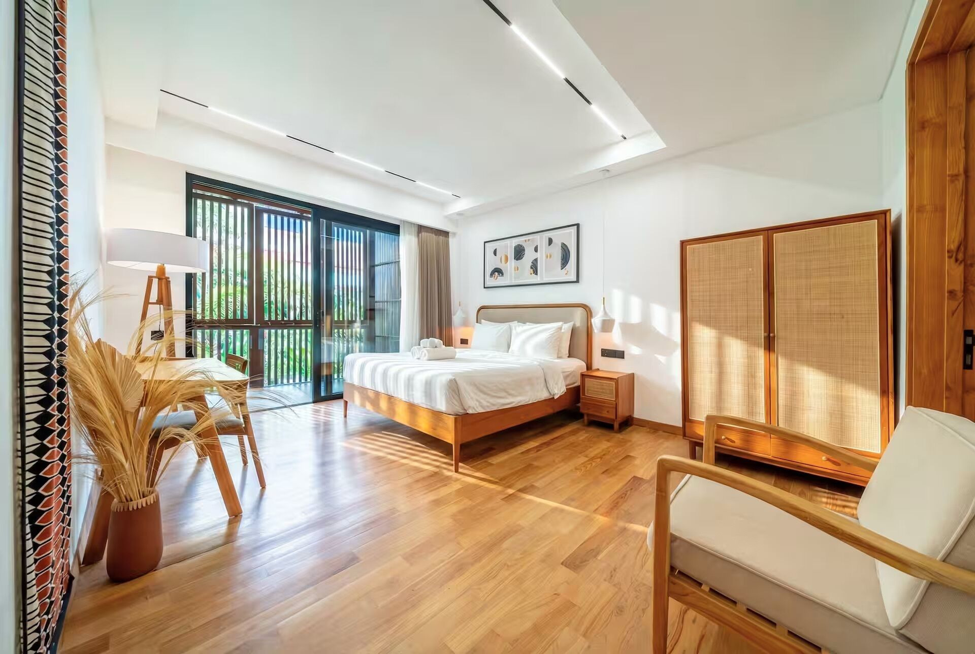 Ein modernes Schlafzimmer mit Bett, Nachttisch, Lampe und Blick auf Grün hinter dem Fenster.
