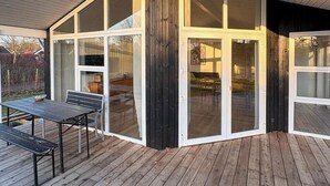 Um edifício moderno com grandes portas de vidro, um deck de madeira e uma área de varanda coberta.