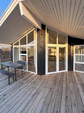 A modern building with large glass doors, a wooden deck, and a covered patio area. - Holiday home close to beach near Norsminde (Odder)