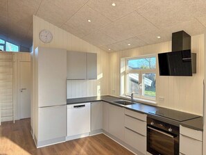 A kitchen with white cabinetry, a built-in oven, a dishwasher, and a window with a view of the outdoors. - Holiday home close to beach near Norsminde (Odder)