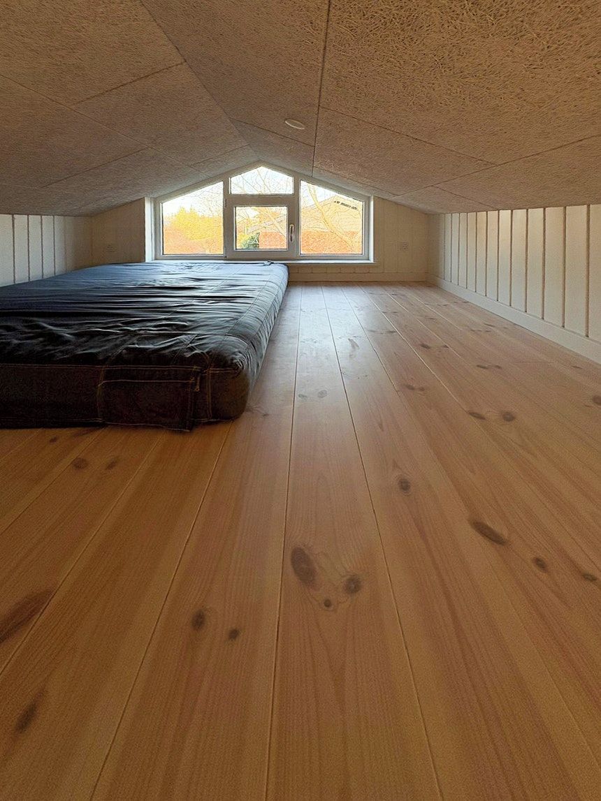 Ein Zimmer mit schrägem Dach, Holzboden, einem Bett und einem Fenster mit Blick.