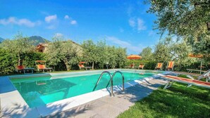 Une piscine entourée d’arbres, avec des chaises longues et des parasols, et une montagne en toile de fond.