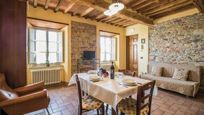 Un coin repas avec une table dressée pour quatre personnes, des murs en pierre, un plafond en bois et un canapé à l’arrière-plan.