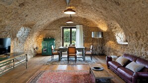 Quarto com paredes de pedra, uma mesa de jantar de madeira, cadeiras, um sofá de couro e uma televisão.