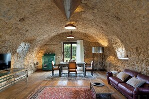 Ein Zimmer mit Steinwänden, einem Holzesstisch, Stühlen, einem Ledersofa und einem Fernseher.