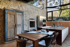 A rustic kitchen with stone walls, wooden cabinetry, and a large island with bar stools. - Barn with stone vaults between Verona and Garda (Negrar di Valpolicella)