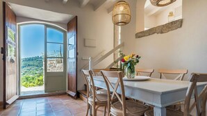 A dining area with a table and chairs, a view through an open door, and a hanging light fixture. - Design stone house in Mallorca's Sóller valley (Soller)