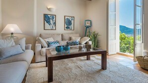 A living room with a sofa, coffee table, and artwork on the wall. - Design stone house in Mallorca's Sóller valley (Soller)