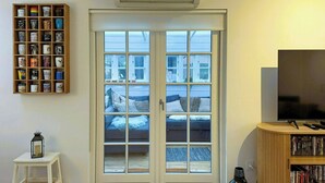 Habitació amb porta corredissa de vidre que dona a un balcó, una estantalla, una taula petita blanca i una televisió.