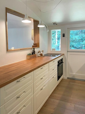 A kitchen with wooden countertops, white cabinets, a large mirror, pendant lighting, and a view of trees through a window. - Renovated holiday home near Als Odde Beach (Hadsund)