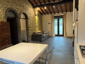 Ein Zimmer mit Steinwänden, ausgestattet mit einer Couch, einem Tisch und einer Küchenzeile mit Herd.