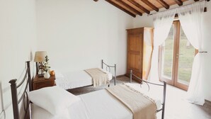 Une chambre à coucher avec un lit, une table de chevet avec une lampe, une armoire en bois et une fenêtre avec des rideaux.