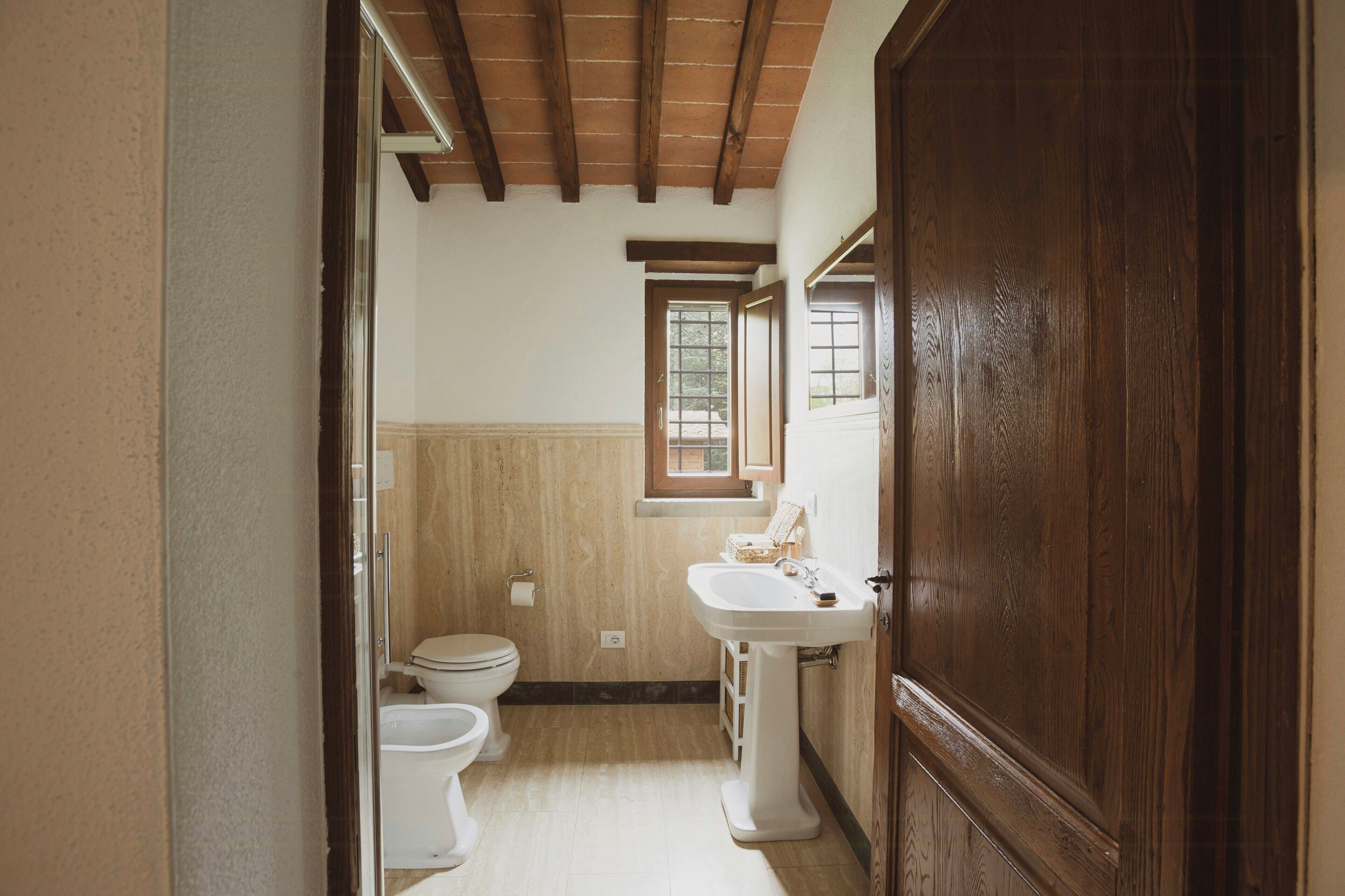 Ein schmales Badezimmer mit Holztür, Waschbecken in Weiß und Toilette.