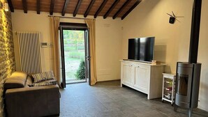Un salon avec un canapé, un téléviseur, une cheminée et une vue sur l’extérieur, visible à travers une porte.