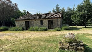 Un bâtiment en pierre avec un toit en tuiles, entouré de pelouse et d’arbres.