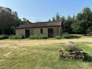 Ein Gebäude aus Stein mit einem Ziegeldach, umgeben von Gras und Bäumen.