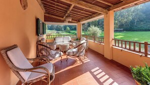 Un patio couvert avec des meubles en osier, une vue sur un terrain de golf et un plafond en bois.