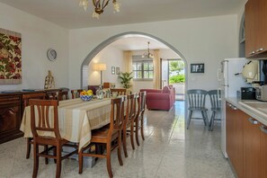 Ein Essbereich mit Tisch für sechs Personen, eine Küche mit Kühlschrank und Mikrowelle sowie ein Wohnbereich mit Sofa und Sesseln.