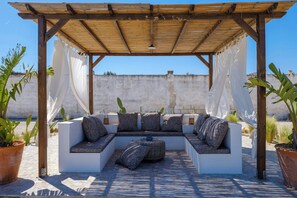 Ein überdachter Außenbereich mit einer Holzpergola, gepolsterten Bänken und Blumentöpfen.