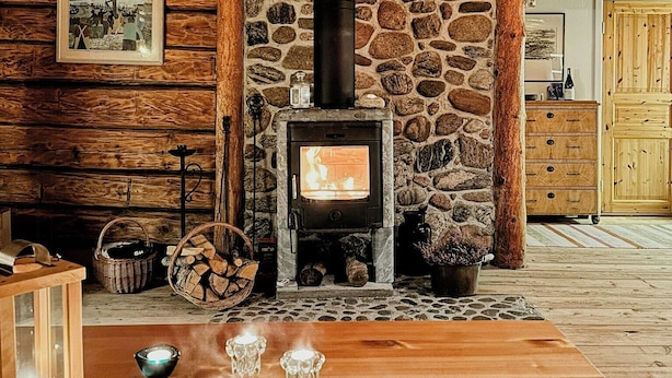 Un interior rústico con chimenea de piedra, vigas de madera, una mesa de madera con velas y un cuadro en la pared.
