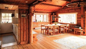 Interior de una cabaña de madera con cocina, comedor y amplias ventanas.