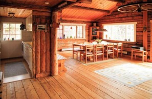 A wooden cabin interior with a kitchen, dining area, and large windows. - Historic timber cottage from 1700s on Hamburgö (Hamburgsund)
