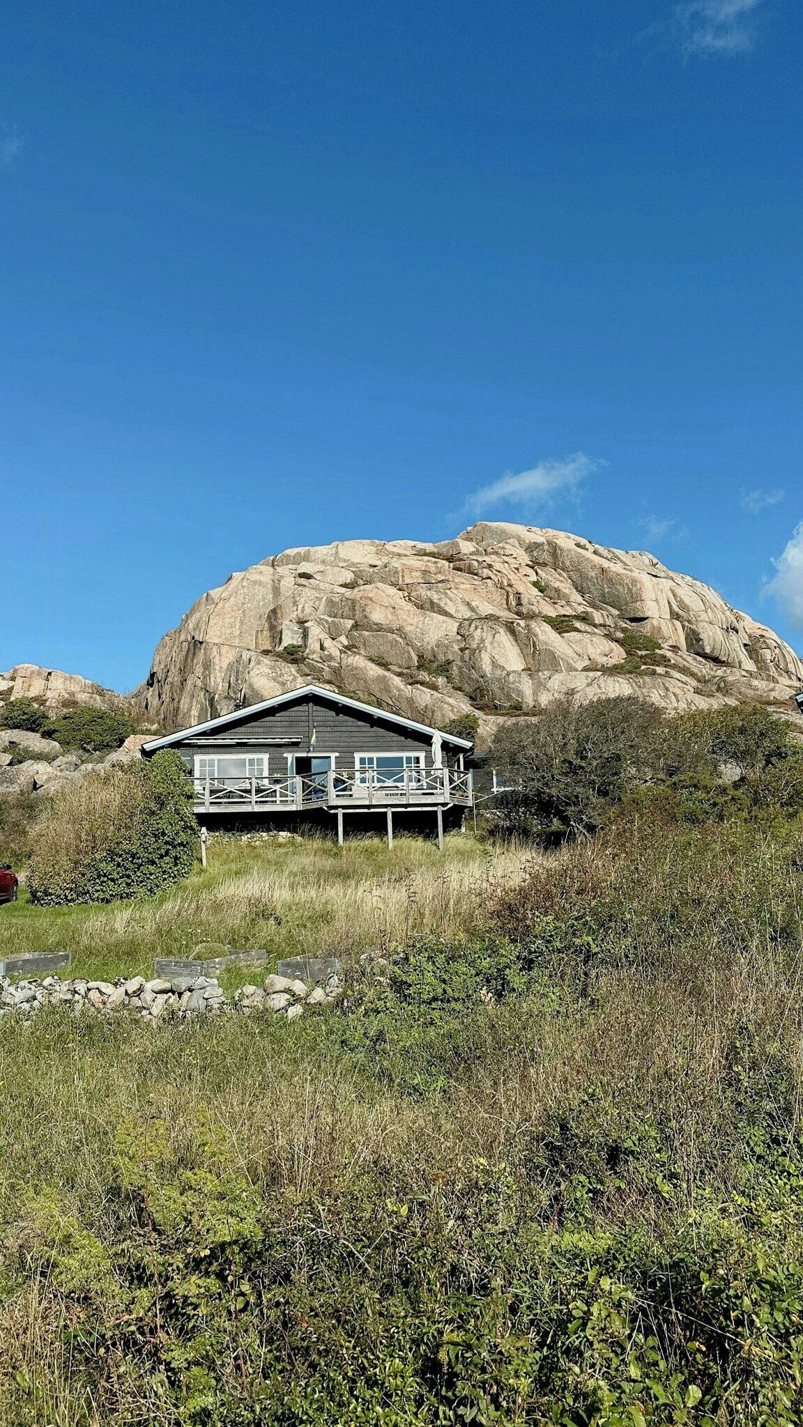 Une cabane dotée d’un balcon, entourée d’un paysage naturel et d’une grande formation rocheuse.