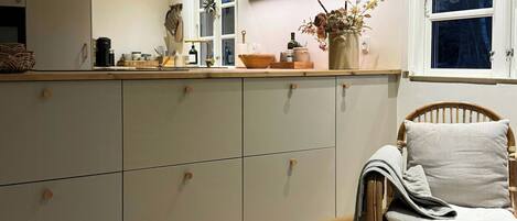 A kitchen with a built-in island, wooden cabinets, and a wicker chair with a cushion.