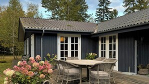 Eine Holzterrasse mit Esstisch und Stühlen, umgeben von Topfpflanzen.