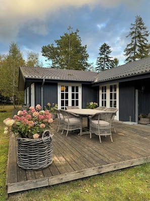 Eine Holzterrasse mit Esstisch und Stühlen, umgeben von Topfpflanzen.