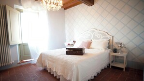 Ein Schlafzimmer mit einem Bett, einer Kommode, einem Heizkörper, einem Fenster mit Vorhängen und einer Pendelleuchte.
