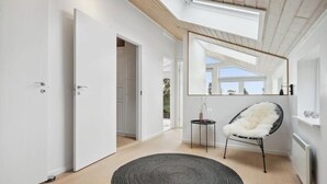 A modern interior with a skylight, a round rug, a chair, and a mirror reflecting the outdoors.