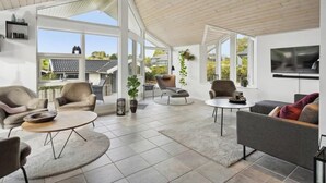 A spacious living area with large windows, a flat-screen TV mounted on the wall, and a variety of seating options including sofas and chairs.