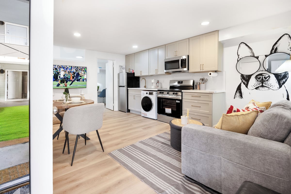 A modern kitchen with a washing machine, microwave, and dining area with a TV.