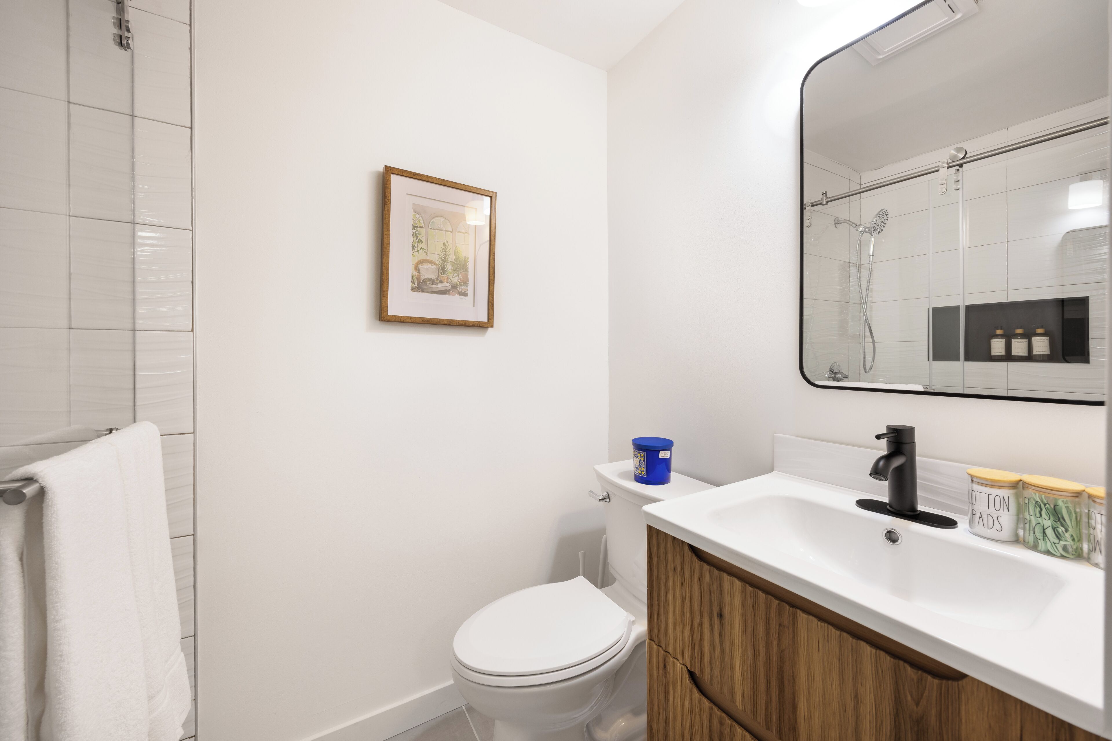 A bathroom with a white toilet, a sink with a mirror above it, and a framed picture on the wall.