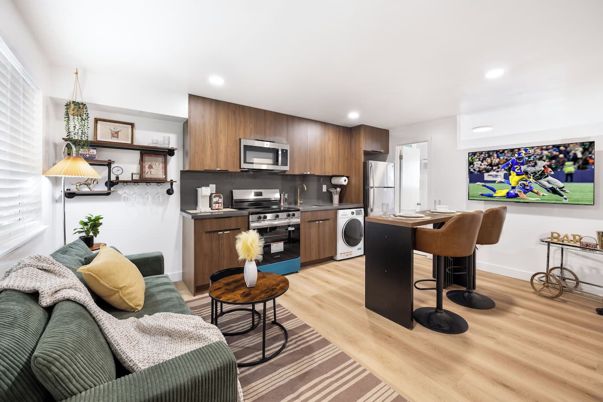 A modern kitchen with a microwave, oven, and refrigerator, a dining area with a table and chairs, and a living room with a sofa and a TV.