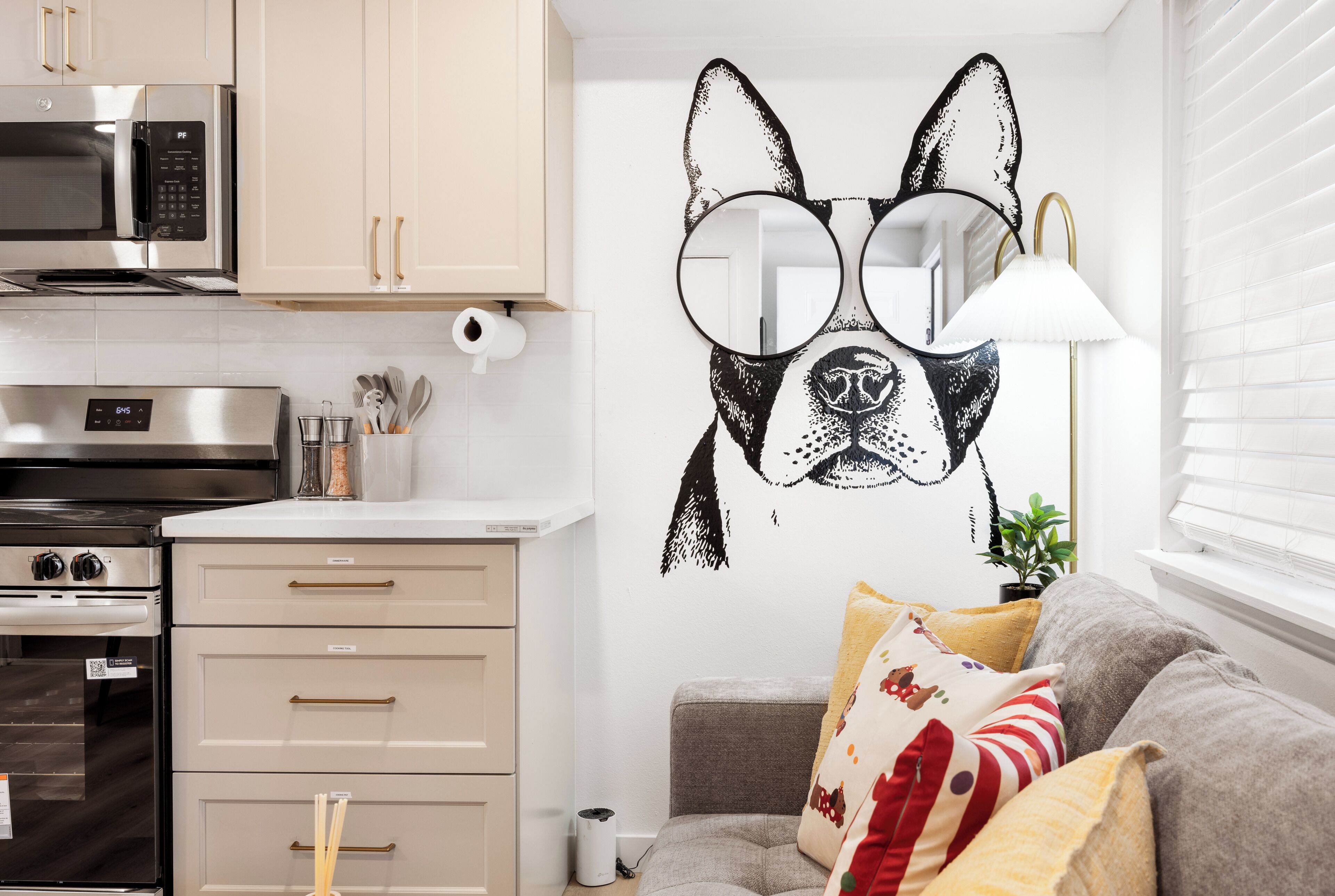A kitchen with modern appliances, a wall art of a dog, and a grey sofa with patterned cushions.