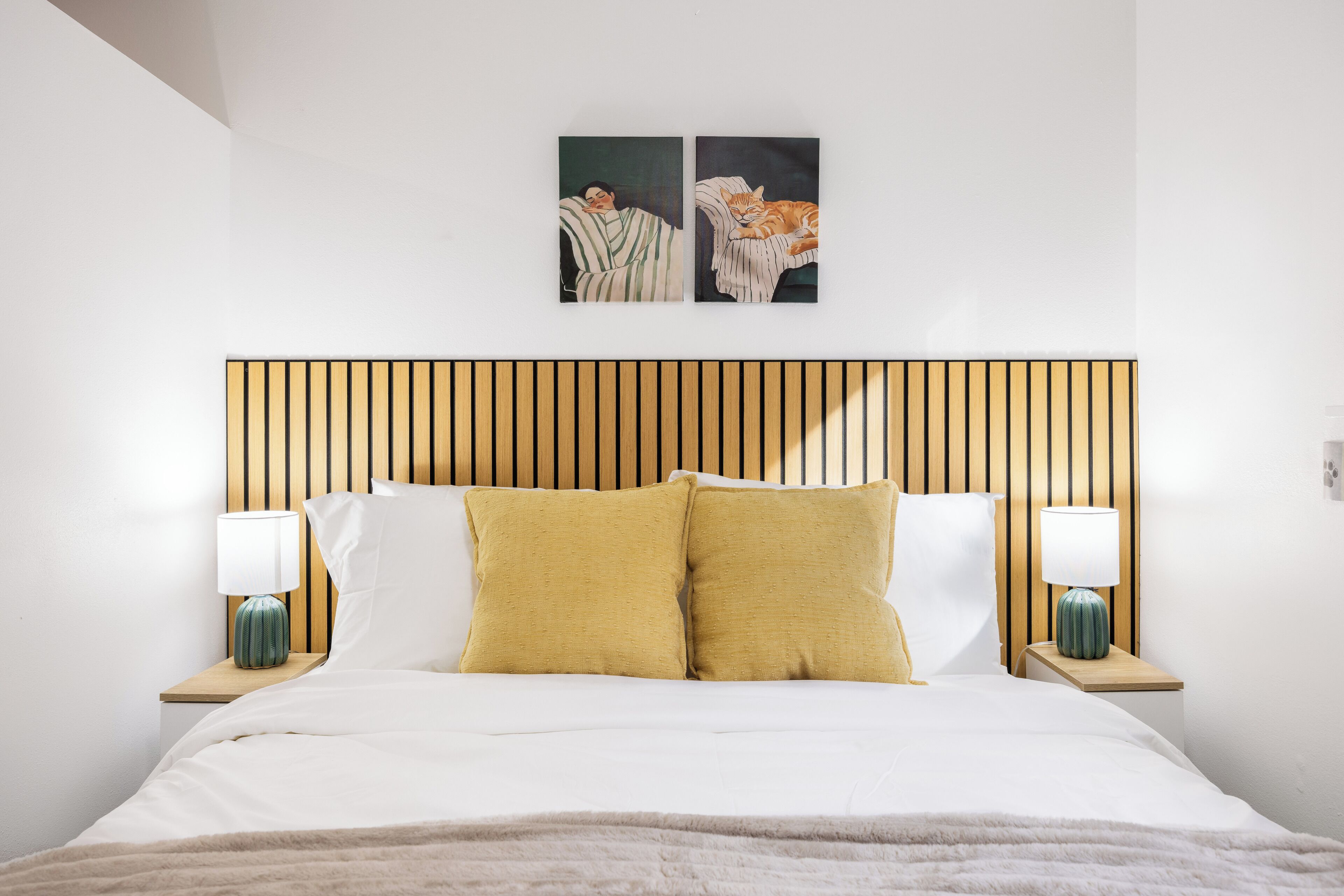 Una cama con cabecera de madera, dos lámparas de noche y dos almohadas.
