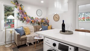 A modern kitchen with a built-in washing machine, a dining area with a white table, and a decorative floral arrangement on the wall. - STAYOO SUITES-Seattle Secret Garden (Seattle)