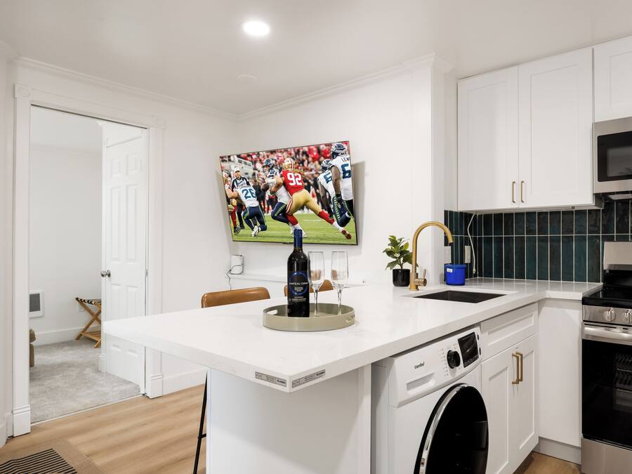 A modern kitchen with a built-in washing machine, a microwave, and a large flat-screen TV mounted above the counter.