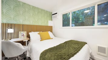 A hotel room with a bed, a desk with a chair, a window with a view of trees, and a wall with a patterned wallpaper.