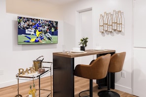 Un comedor moderno con televisor, carrito de bar y botellas de vino.